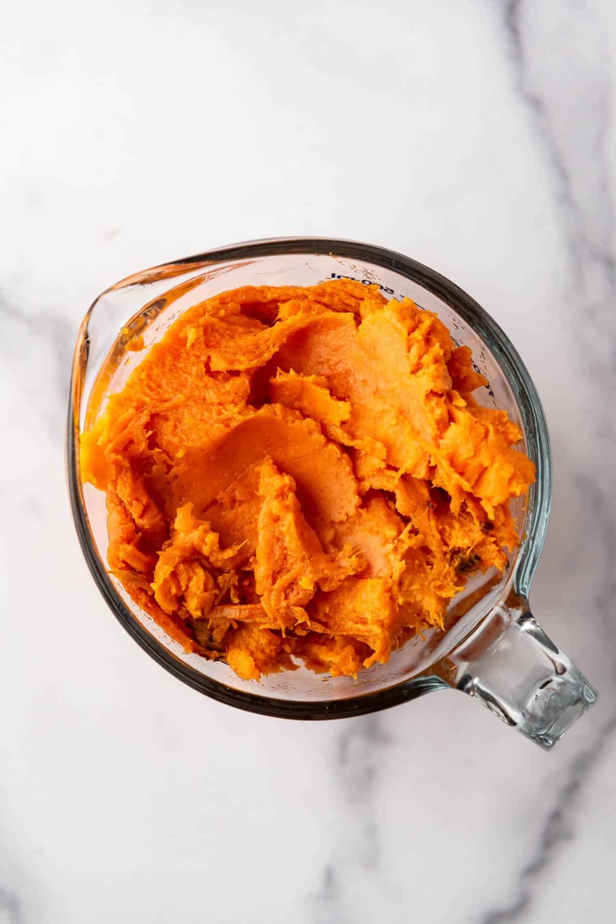Measuring sweet potato puree in a glass measuring cup.