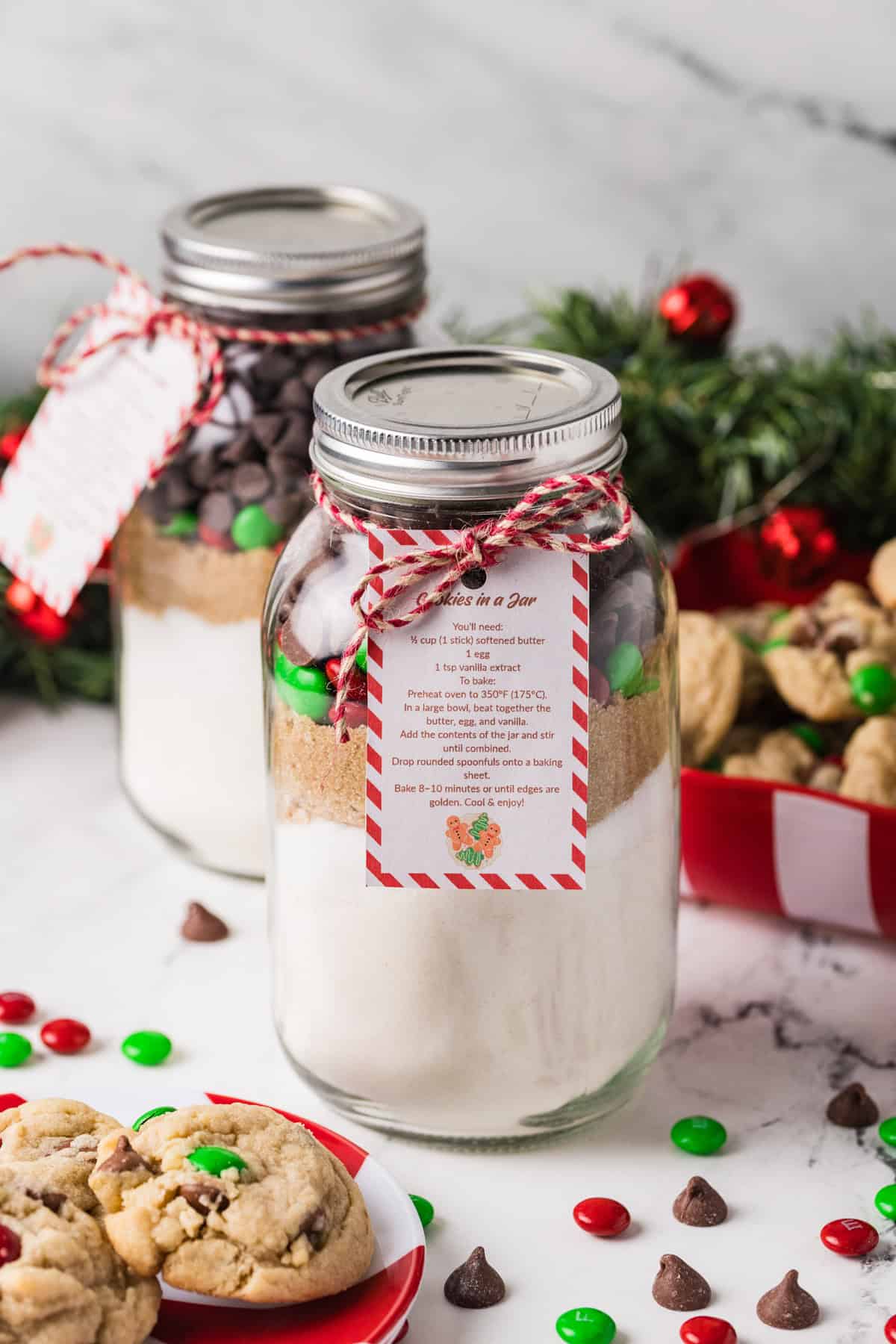 Jars of cookie mix next to a plate of cookies and red & green M&Ms.