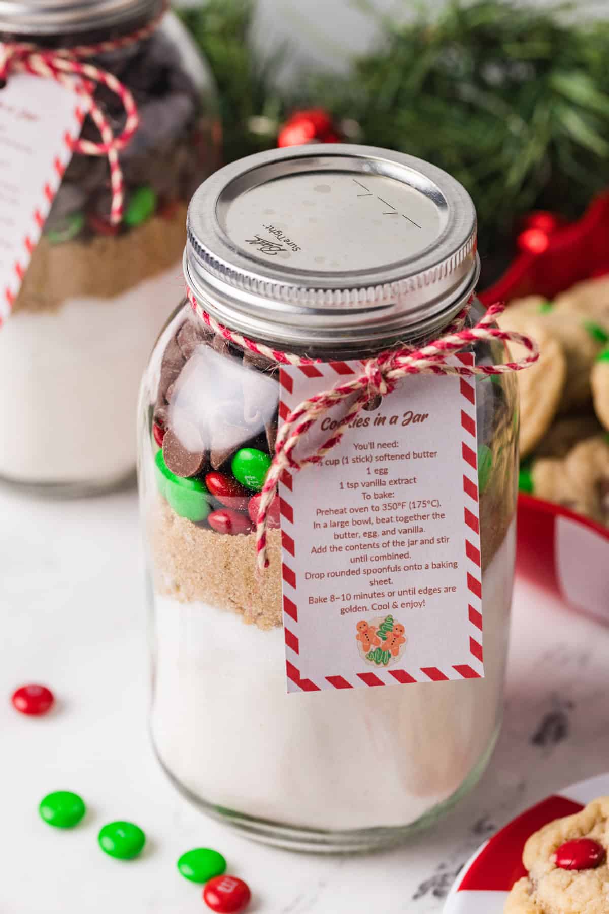 A glass jar filled with ingredients for making Christmas M&M cookies.