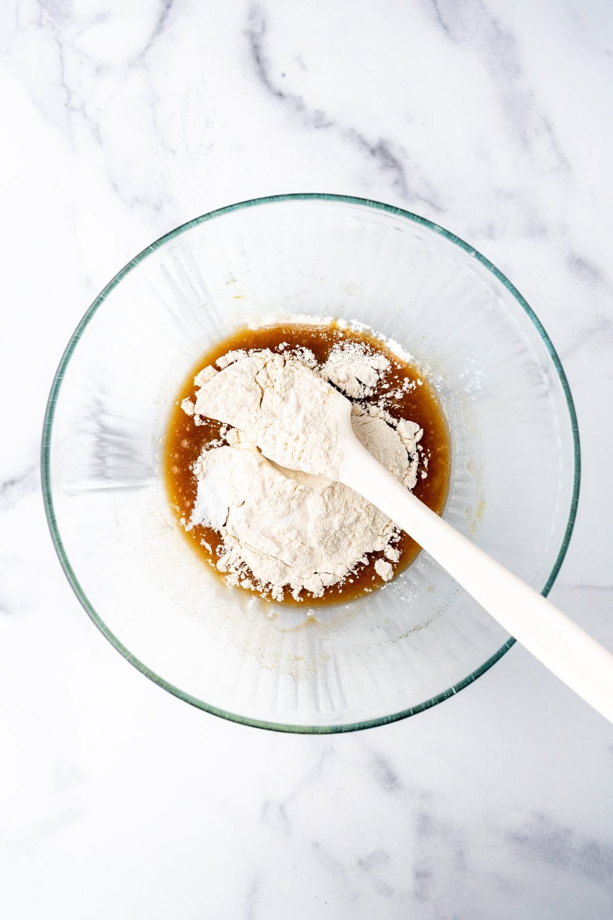 Adding dry ingredients to melted butter, sugar, and eggs in a bowl.