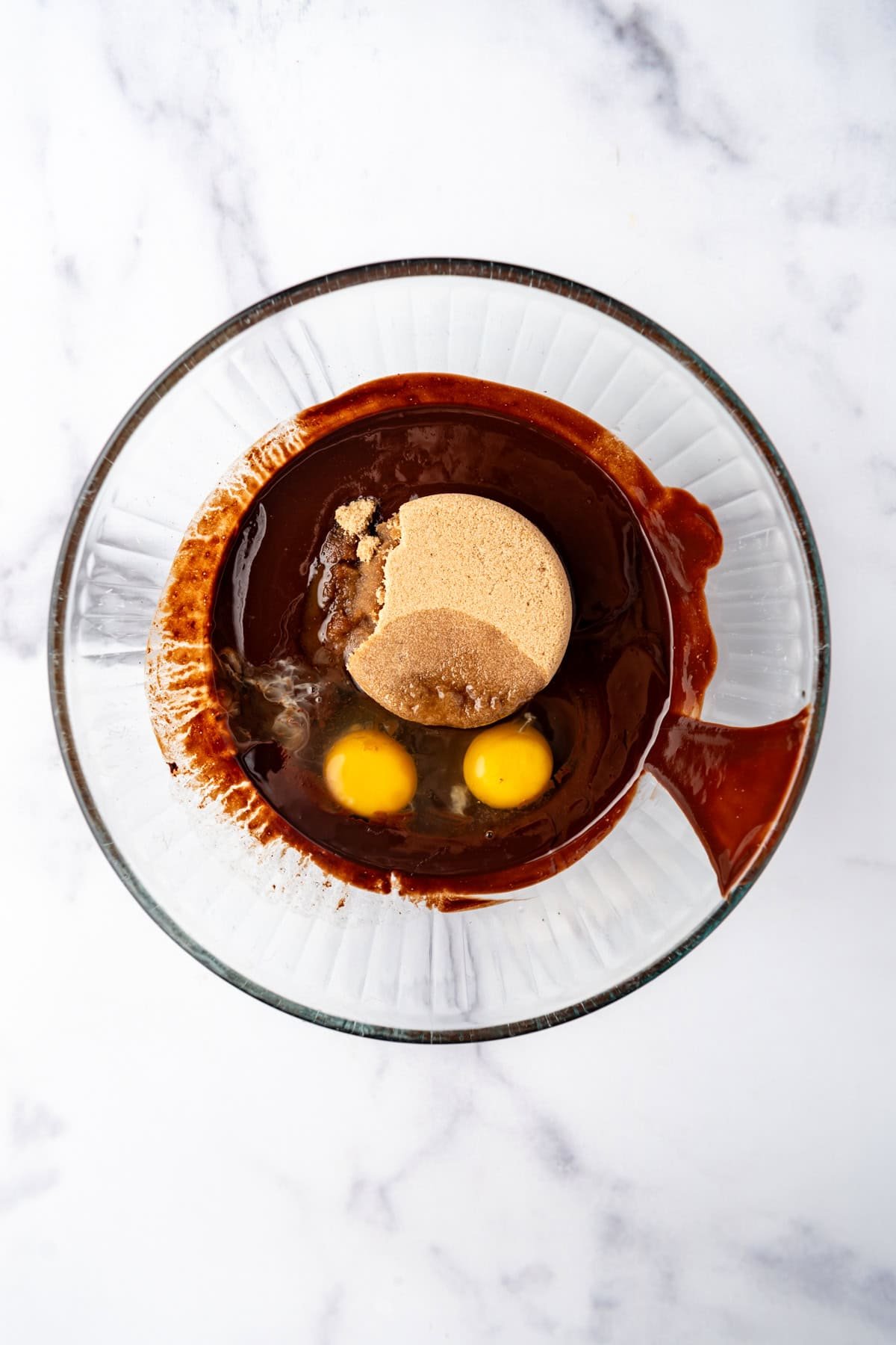 Adding brown sugar and eggs to melted butter and chocolate in a large mixing bowl.