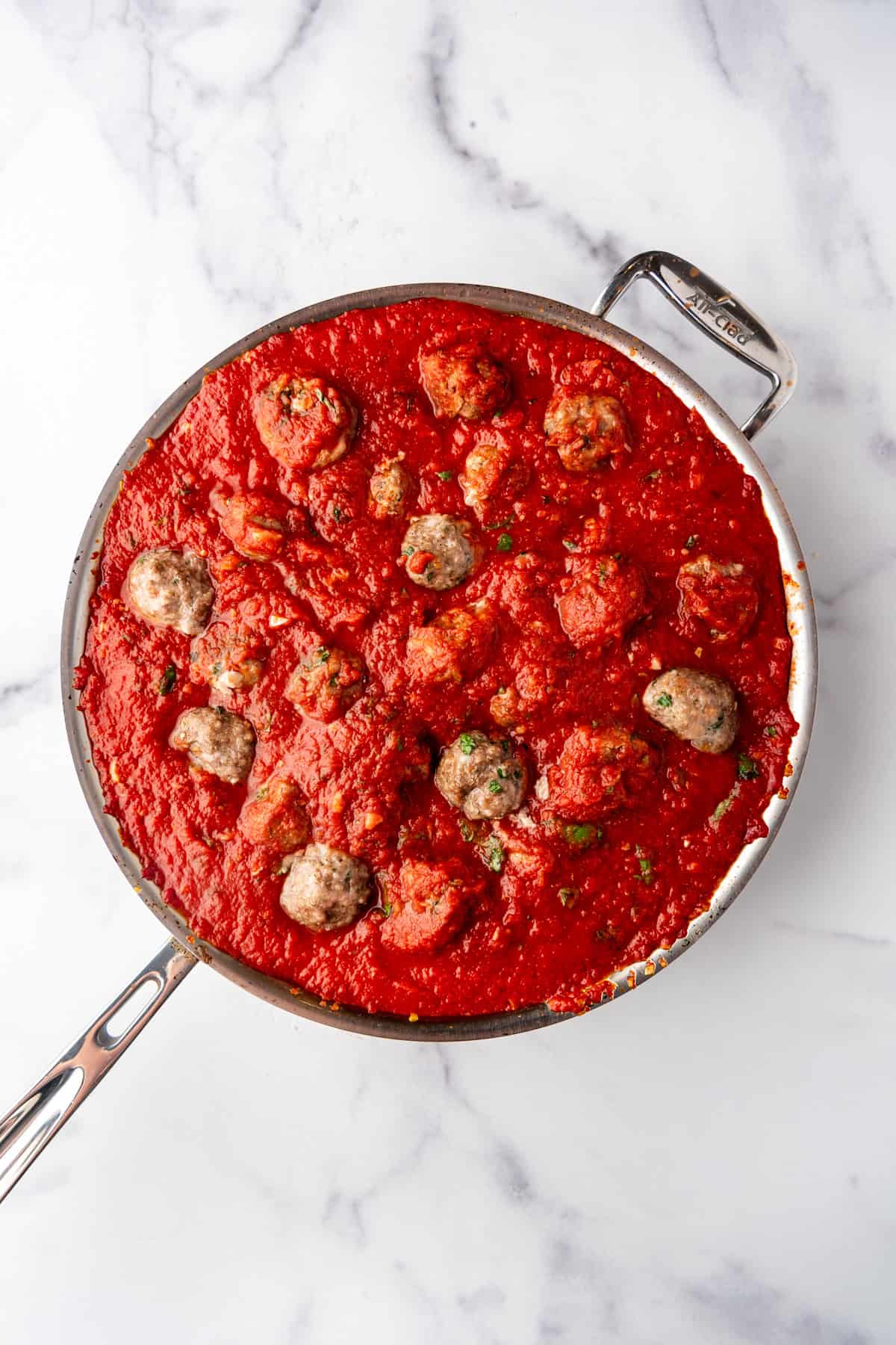 Adding meatballs to marinara sauce in a large pan.