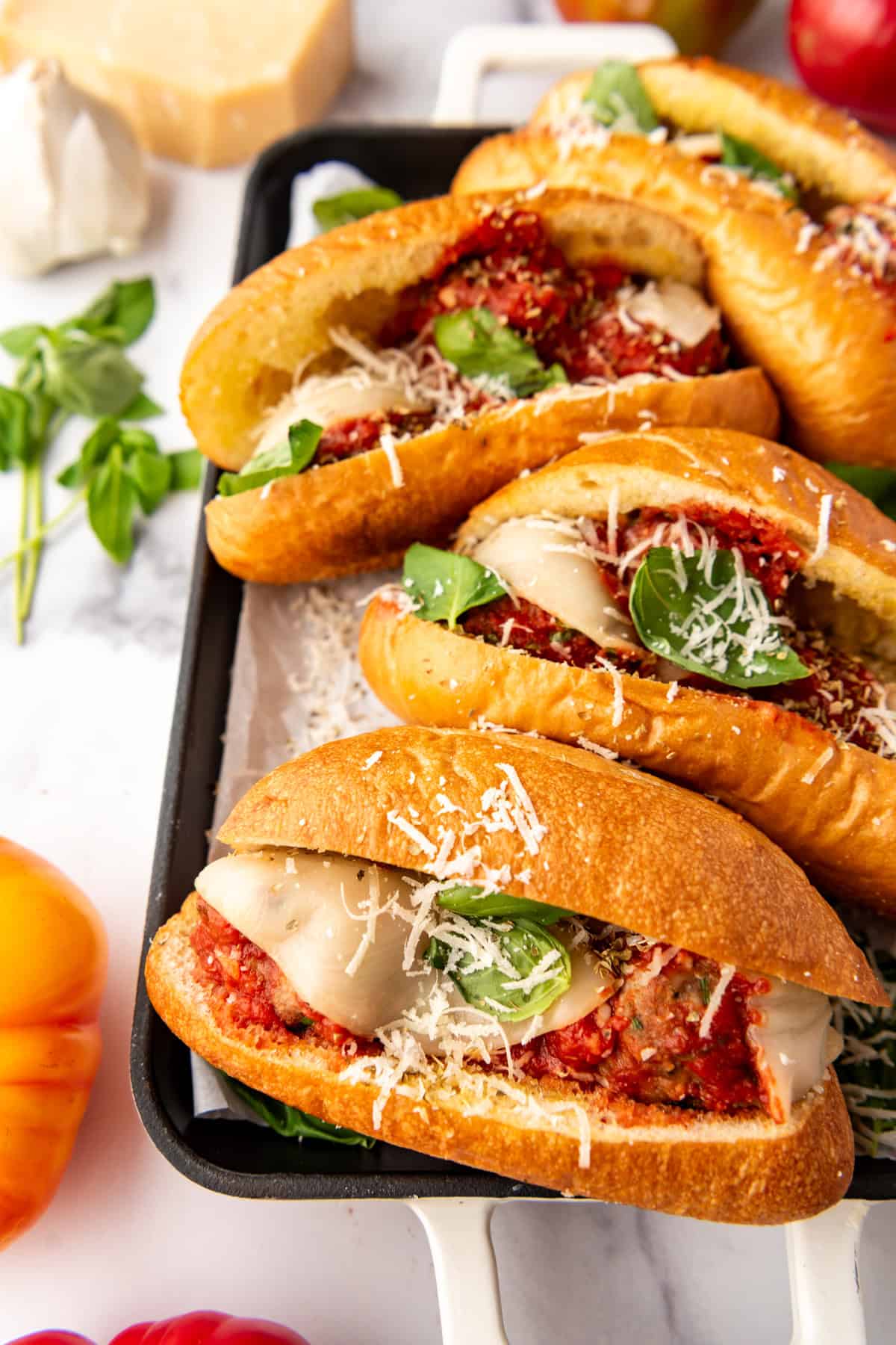 Homemade meatball subs with basil, garlic, tomatoes, and parmesan nearby.