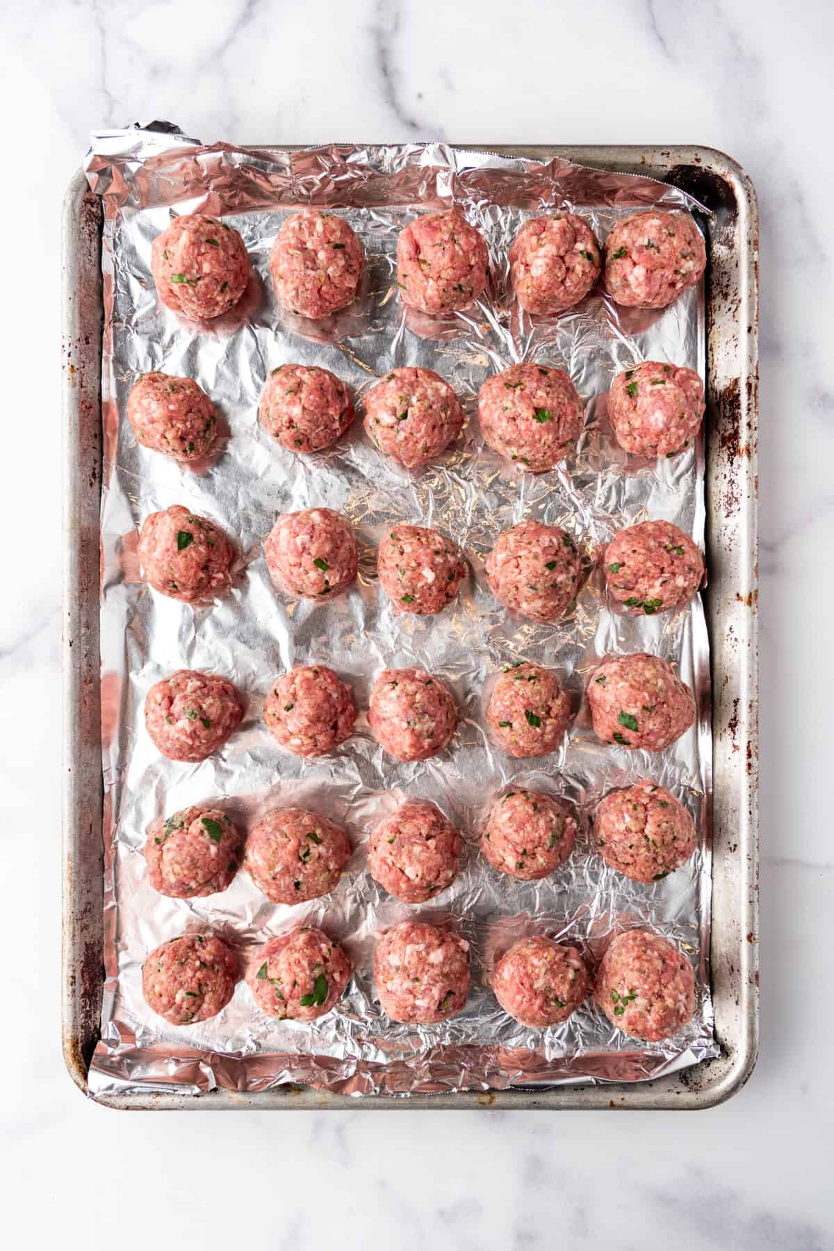 Shaped meatballs on a baking sheet lined with aluminum foil.