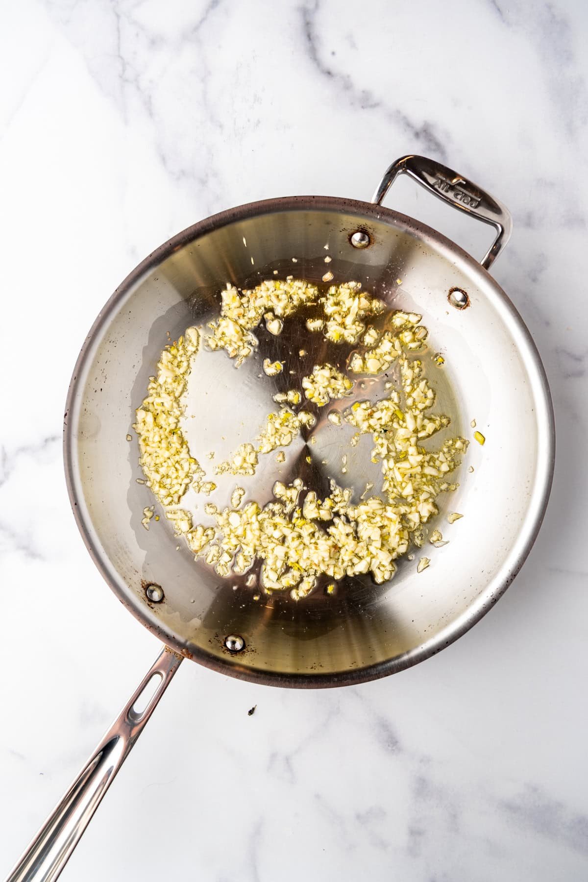 Sauteeing minced garlic in olive oil in a large pan.