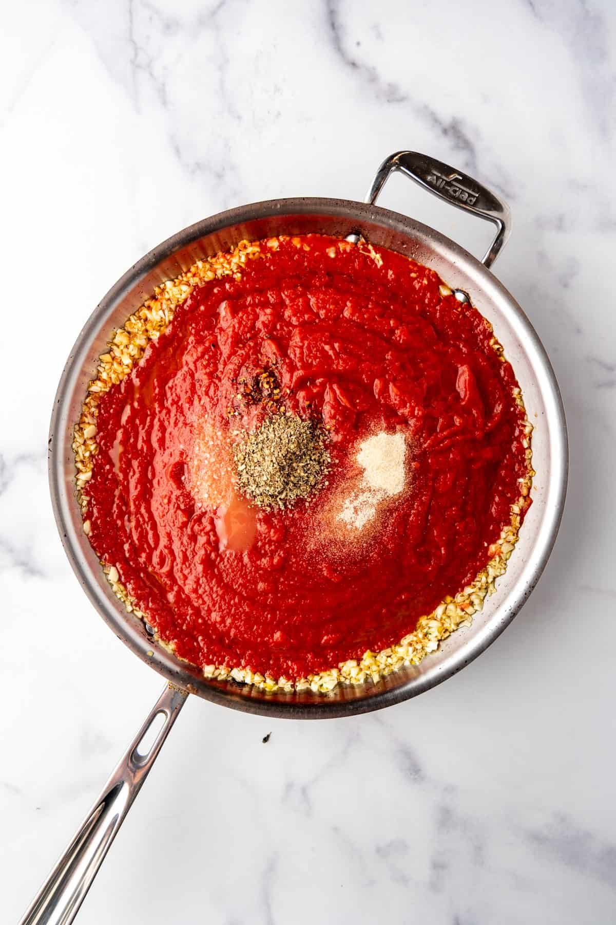 Adding crushed tomatoes and spices to a saucepan with sauteed garlic.