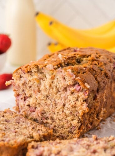 A partially sliced loaf of banana bread with strawberries.