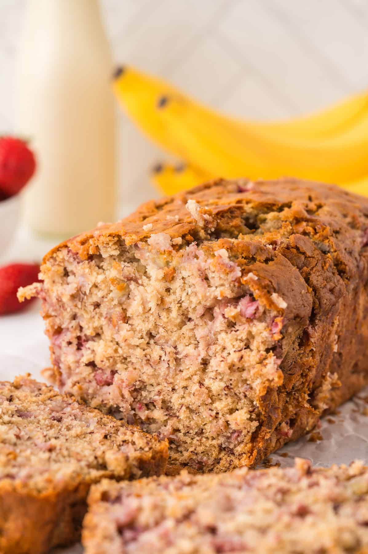 A partially sliced loaf of banana bread with strawberries.