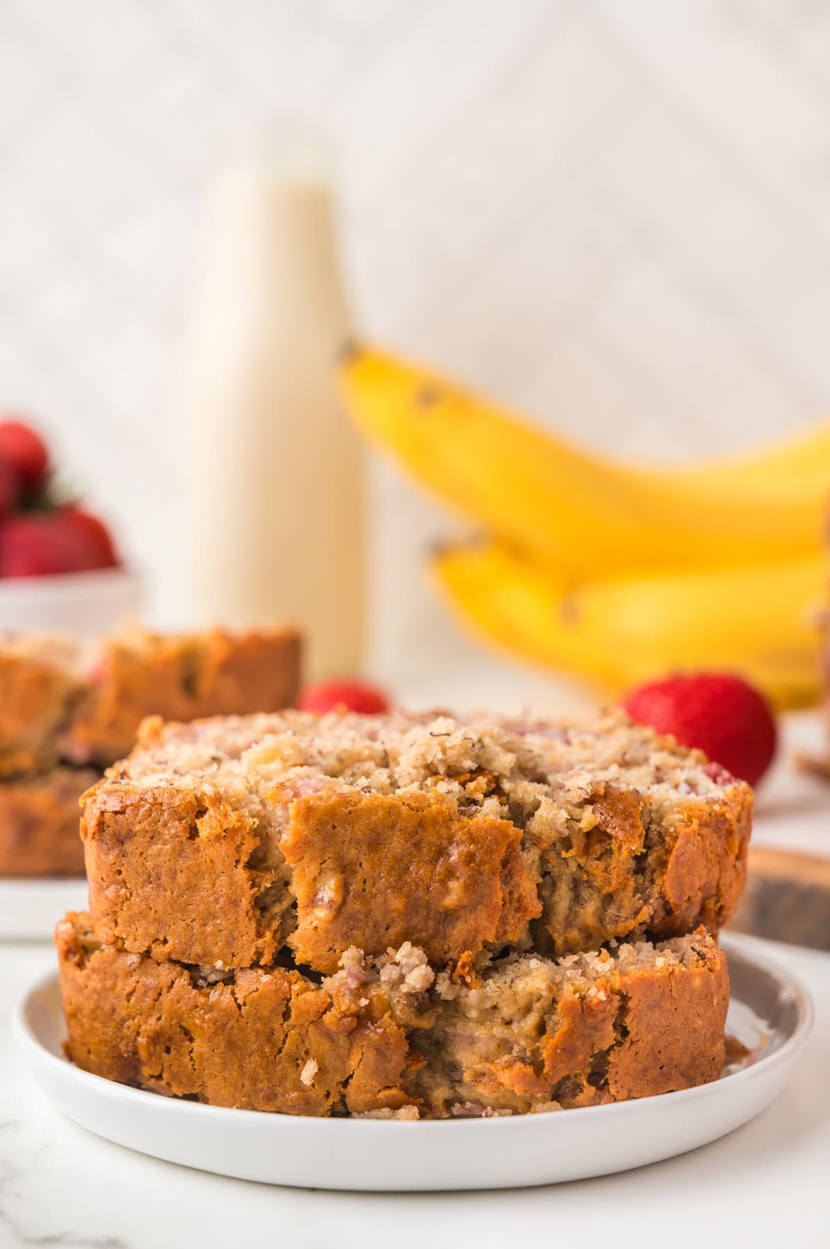 Two slices of strawberry banana bread stacked on a white plate with bananas and milk in the background.