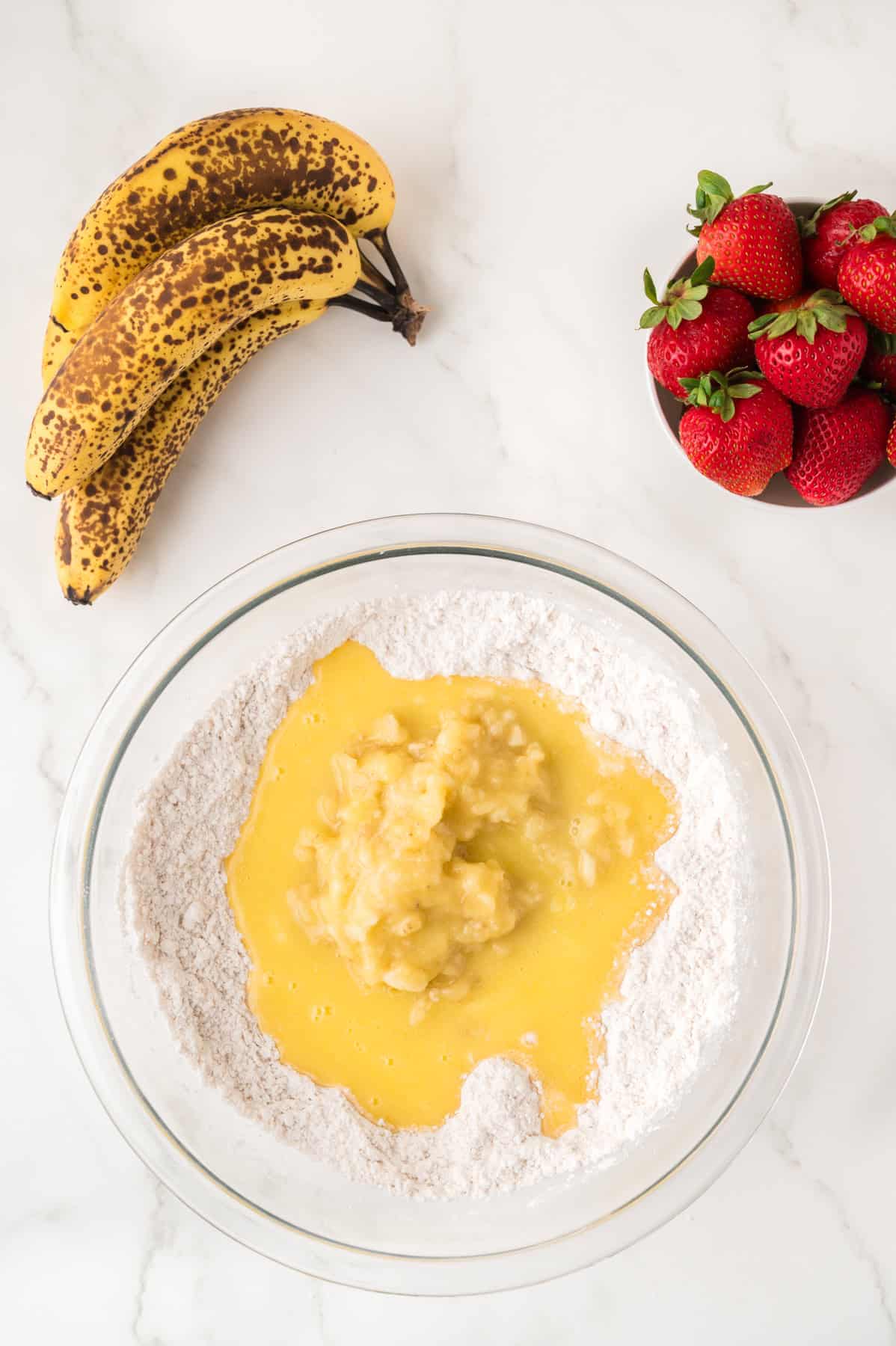 Adding mashed bananas and melted butter to dry ingredients in a bowl.