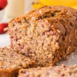 A partially sliced loaf of banana bread with strawberries.