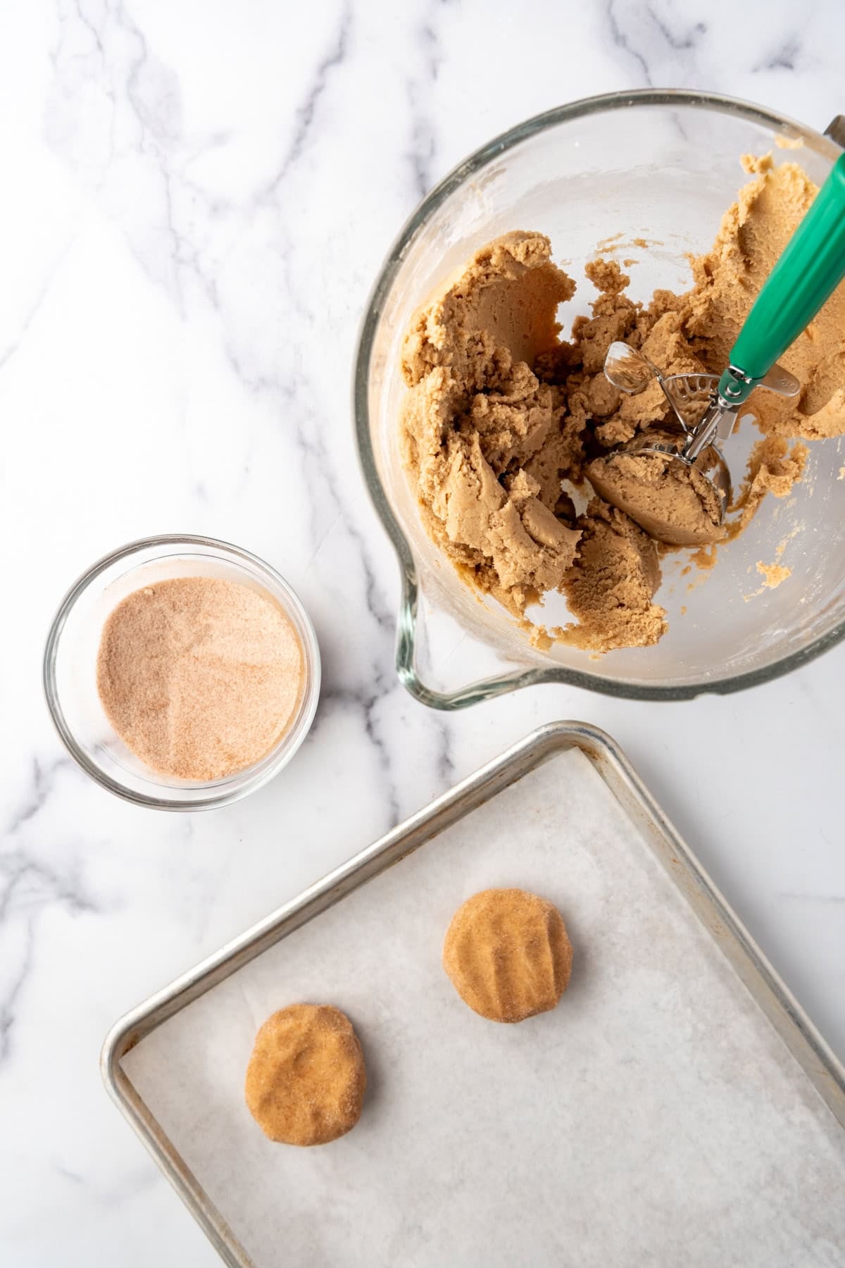 Scooped cookie dough rolled into balls and rolled in cinnamon sugar and placed on a baking sheet lined with parchment paper.