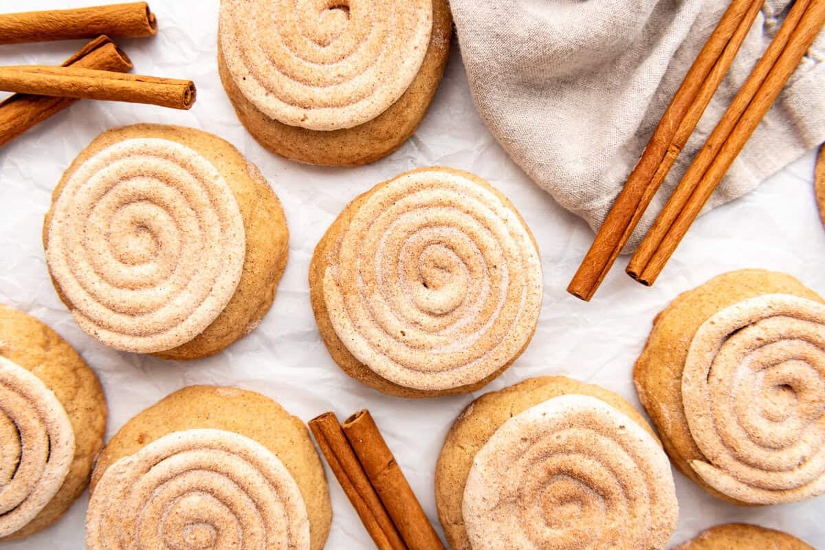 An overhead image of churro cookies with frosting next to cinnamon sticks.