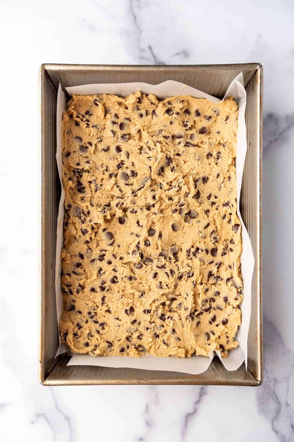Chocolate chip cookie dough spread into a 9x13-inch pan.