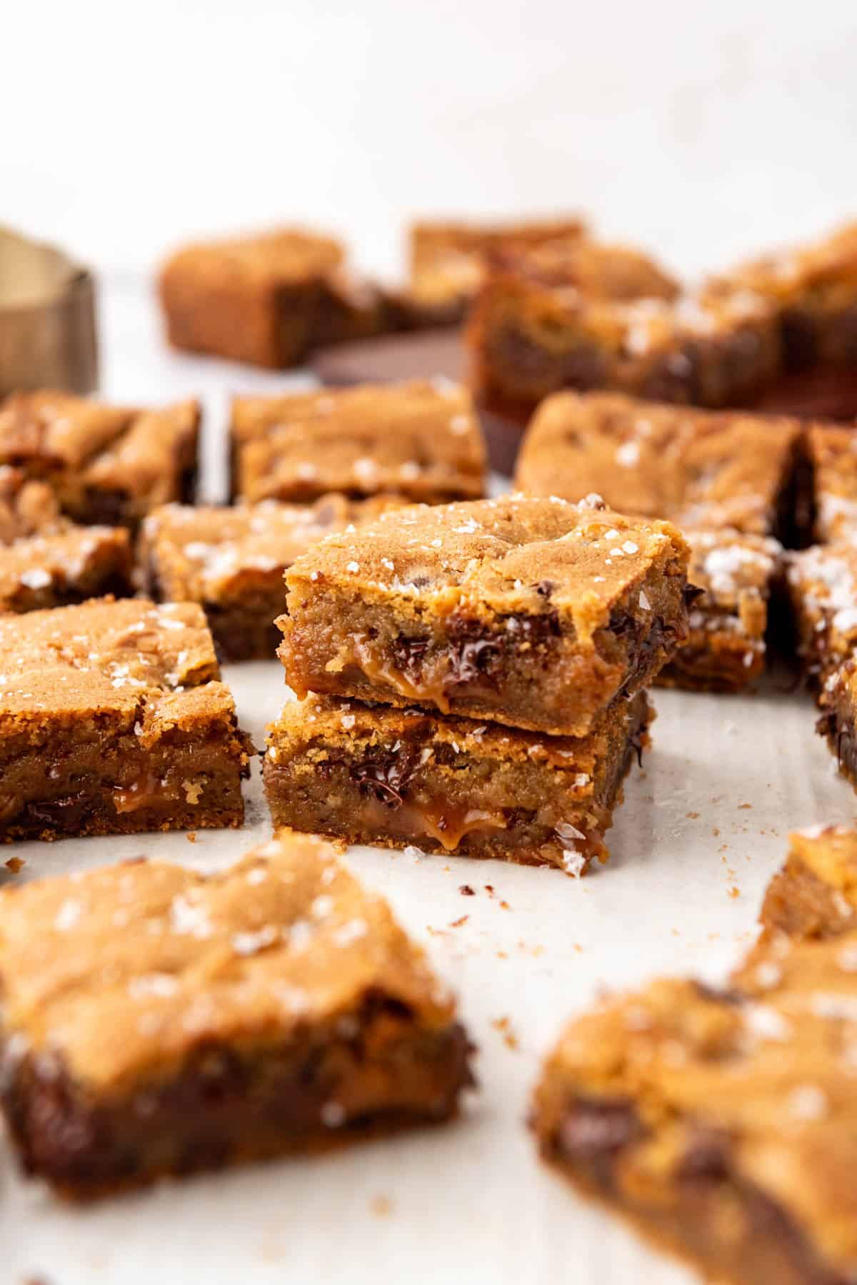 Chocolate chip caramel bars cut into squares and stacked on a white surface.