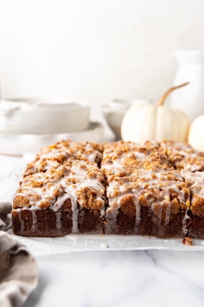An image of glazed pumpkin coffee cake with white dishes and a white pumpkin in the background.