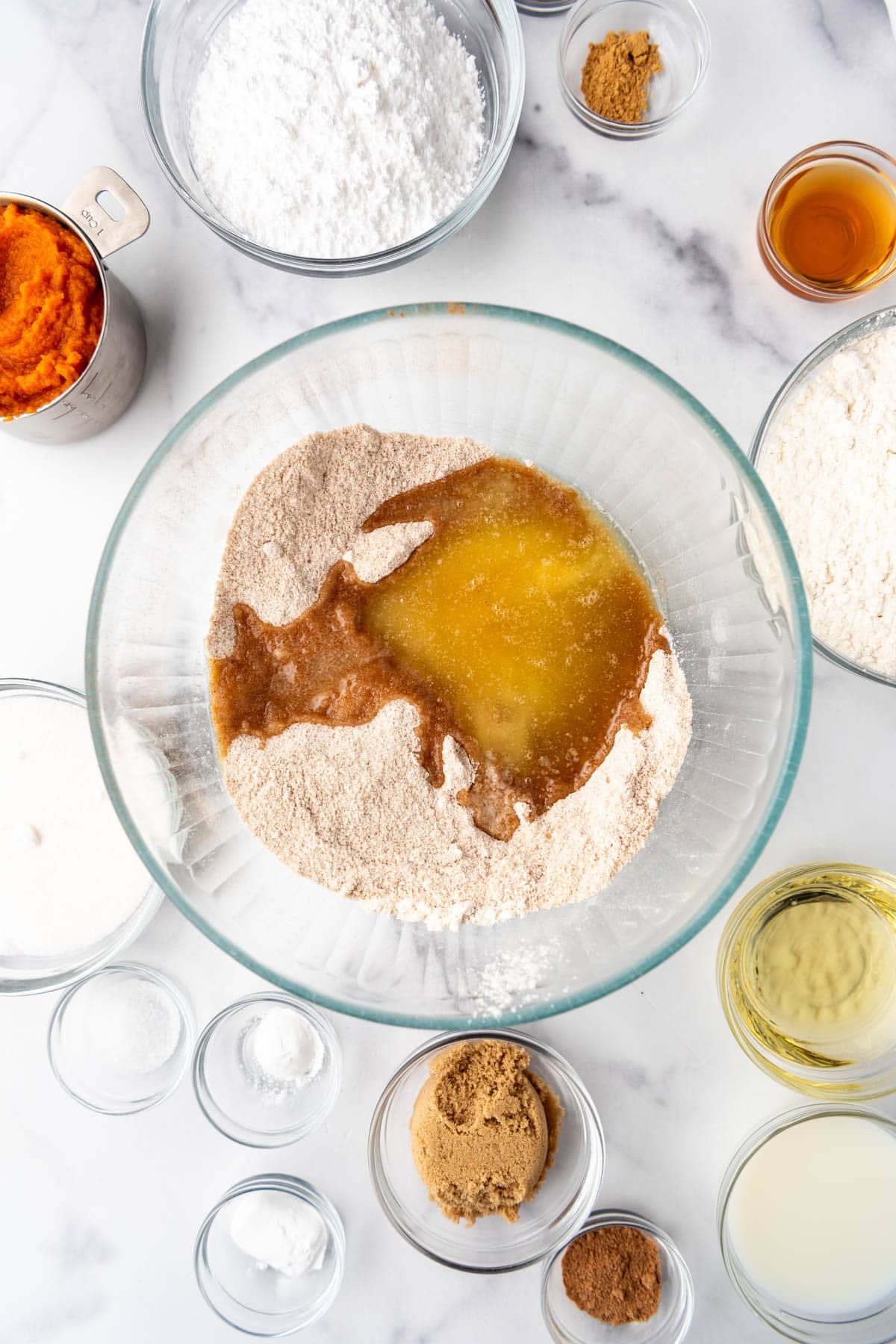Adding melted butter to dry ingredients in a large mixing bowl surrounded by other ingredients.