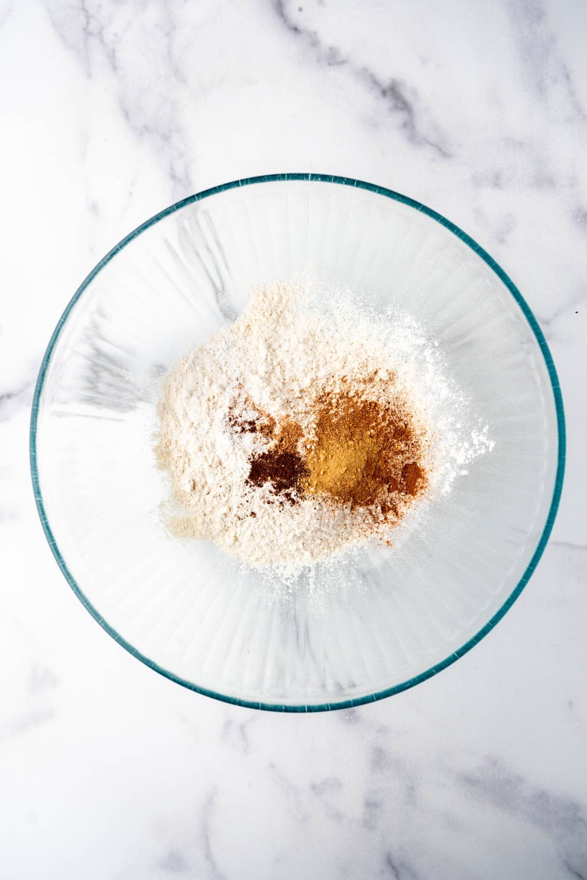 Adding pumpkin spices to flour in a mixing bowl.