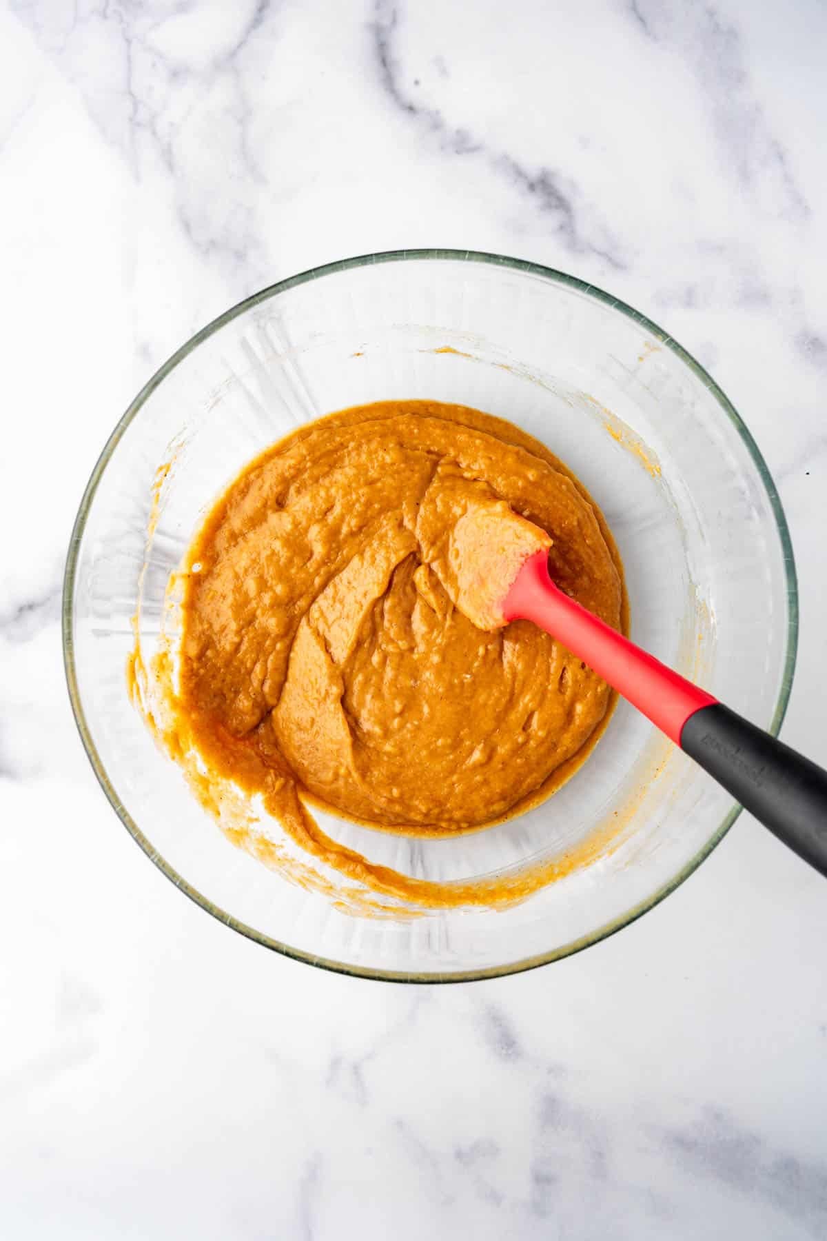 An image of a bowl of pumpkin cake batter with a spatula in it.