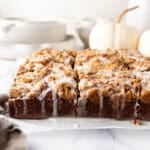 An image of glazed pumpkin coffee cake with white dishes and a white pumpkin in the background.