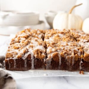 An image of glazed pumpkin coffee cake with white dishes and a white pumpkin in the background.