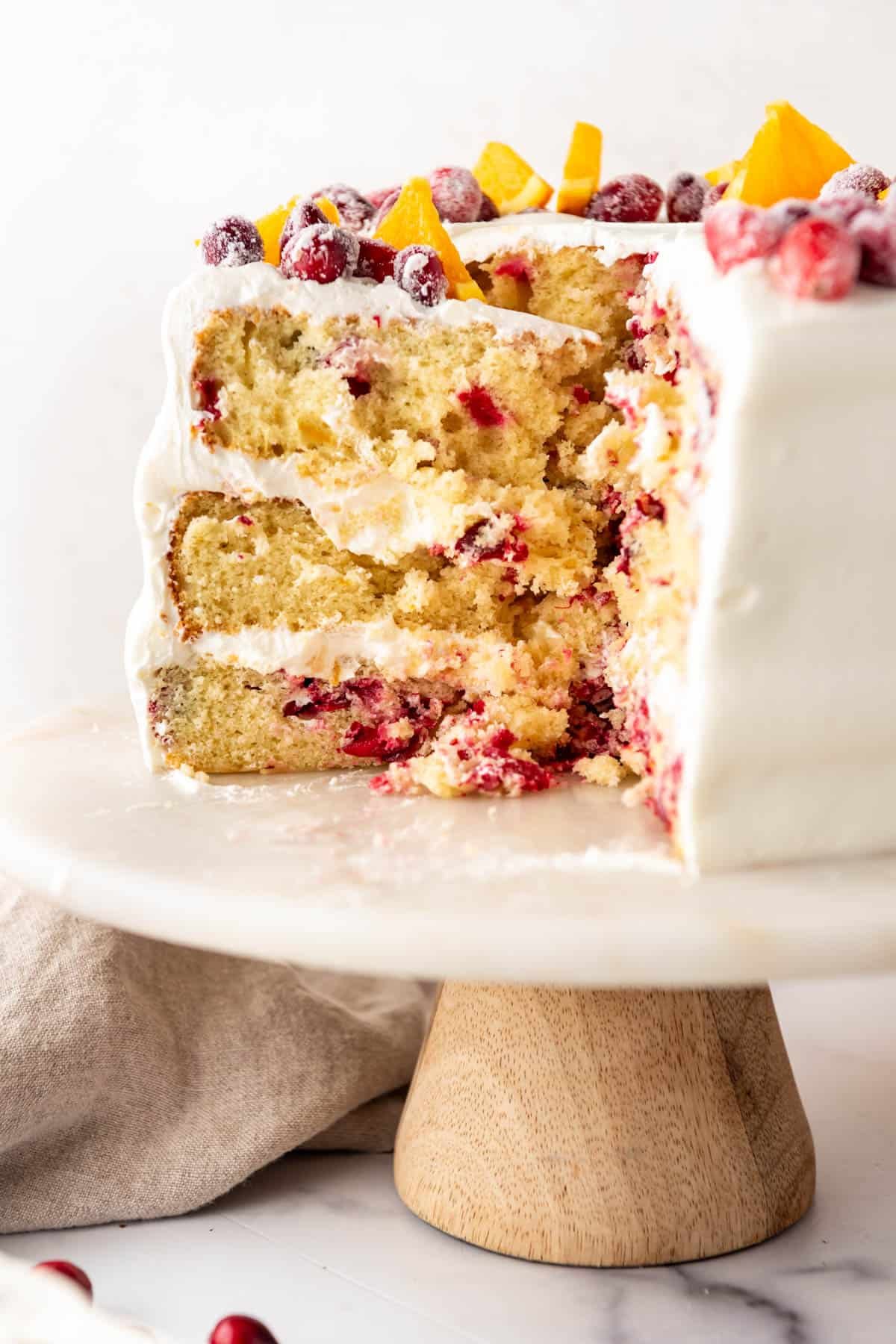 A partially sliced cranberry orange cake on a cake stand.