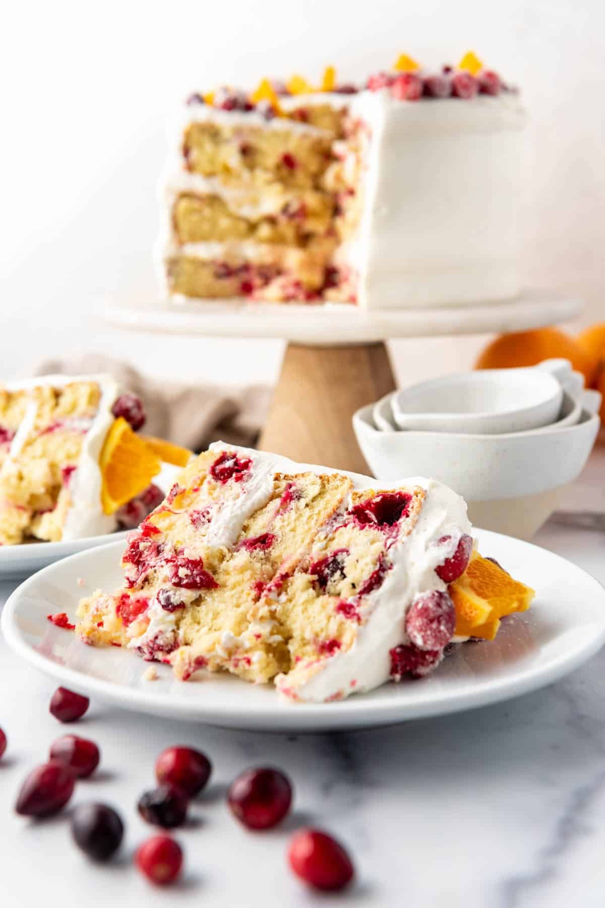 A slice of cranberry orange cake on a white plate with fresh cranberries scattered in front.