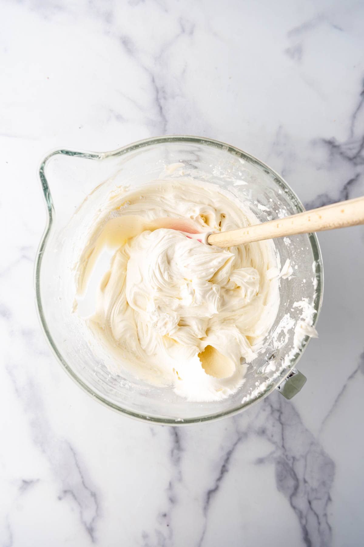 An overhead image of buttercream frosting in a large mixing bowl with a spatula in it.