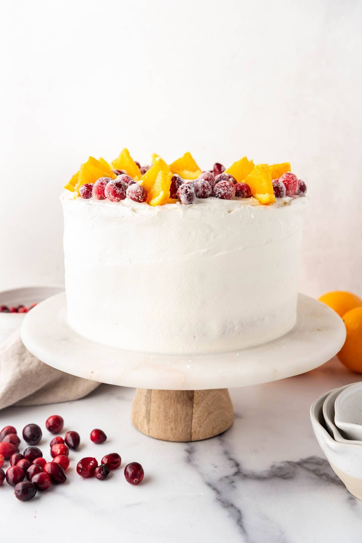 A cranberry orange cake with cream cheese frosting, orange slices, and candied cranberries on top.