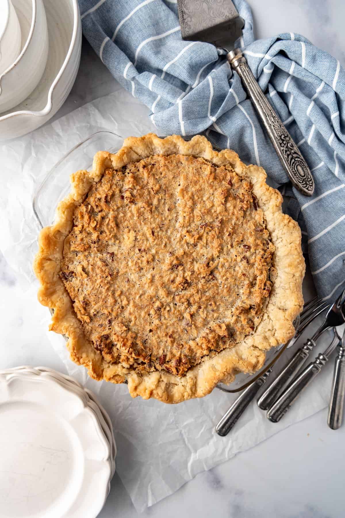 An image of a baked sawdust pie next to forks, plates, and a blue striped cloth napkin.