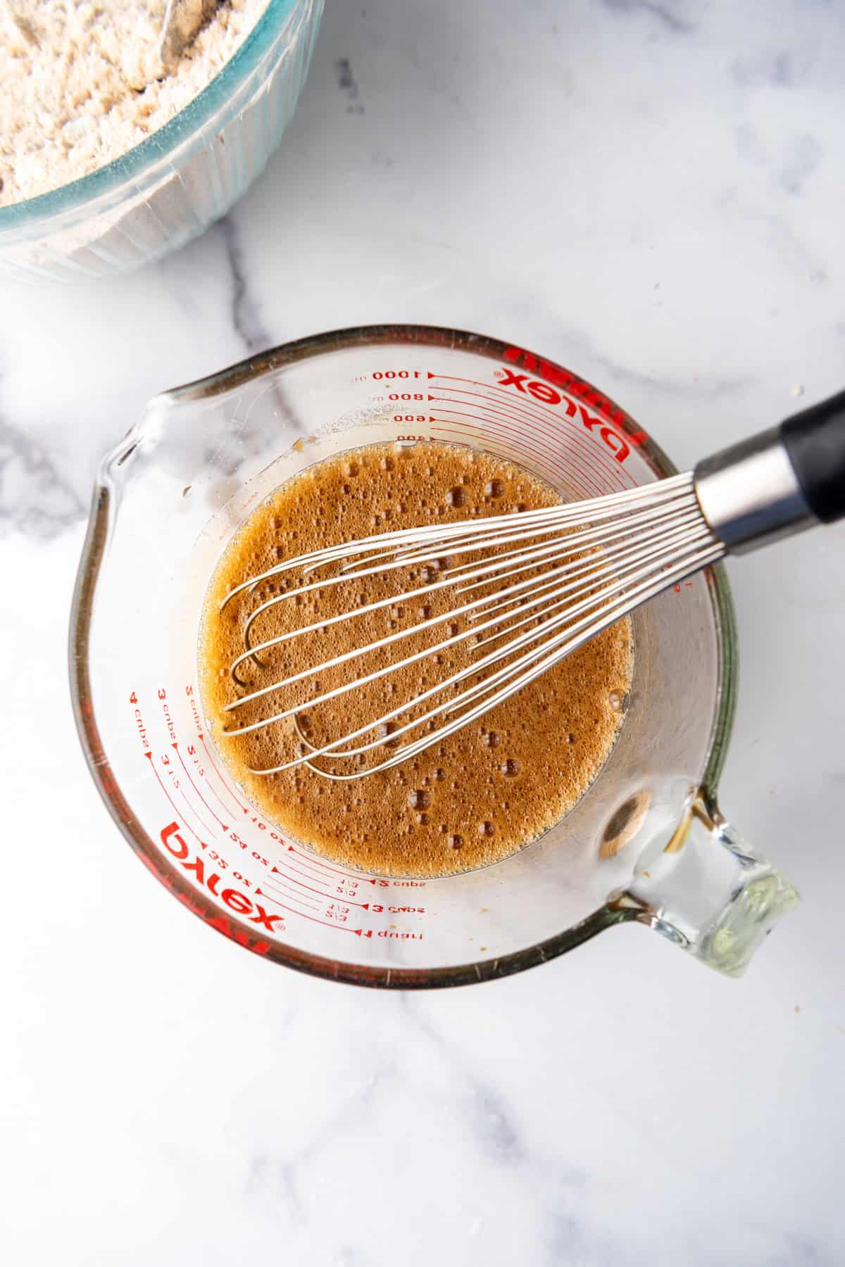 A whisk in a bowl of foaming molasses, baking soda, and hot water.