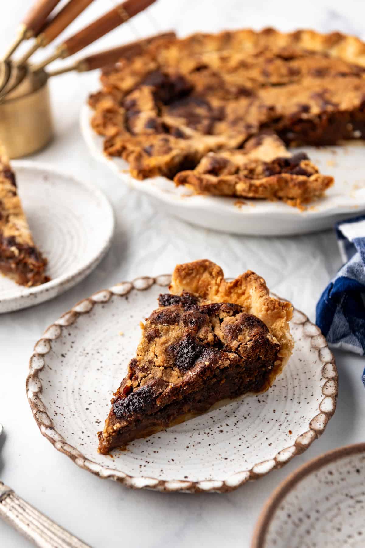 A slice of shoo fly pie on a plate in front of the rest of the pie.