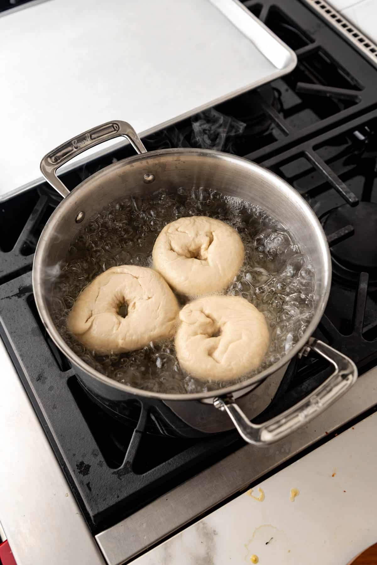 An image of three bagels in boiling water on the stovetop.