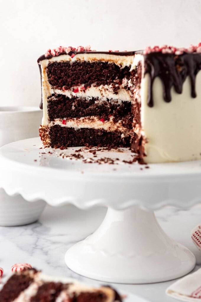 A cross section of a partially sliced peppermint bark cake on a white cake stand.