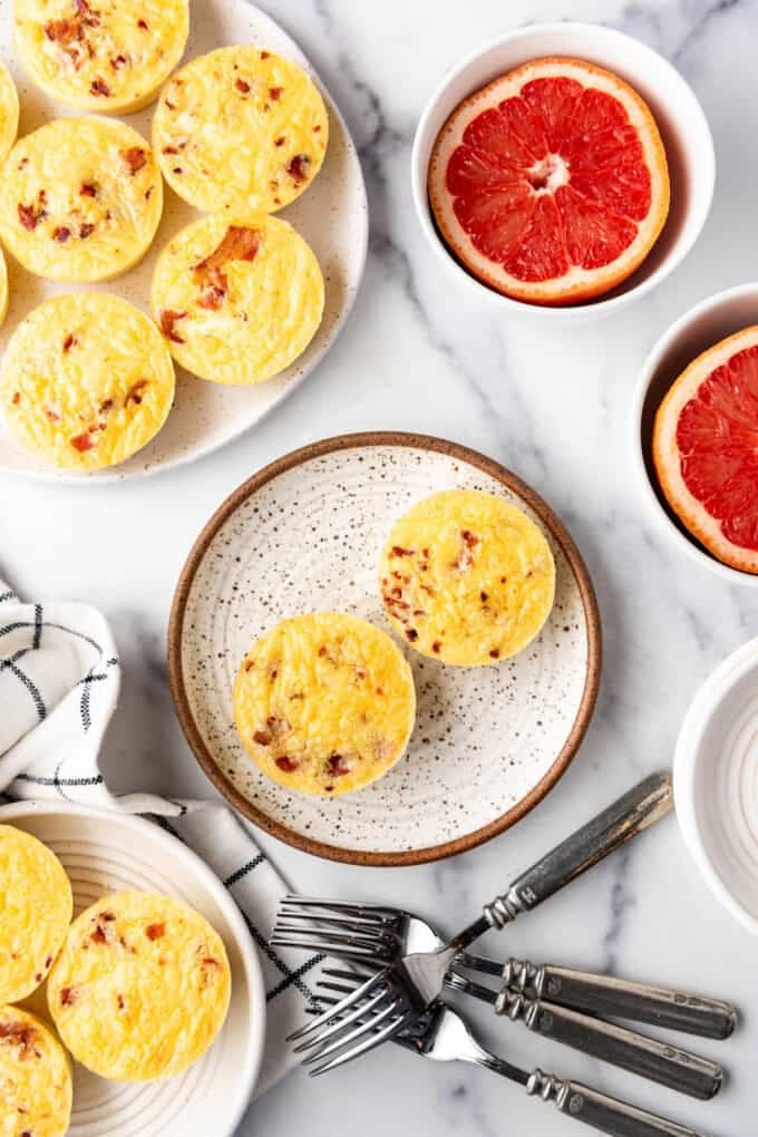 An overhead image of coypcat starbucks egg bites on plates next to forks and grapefruit.