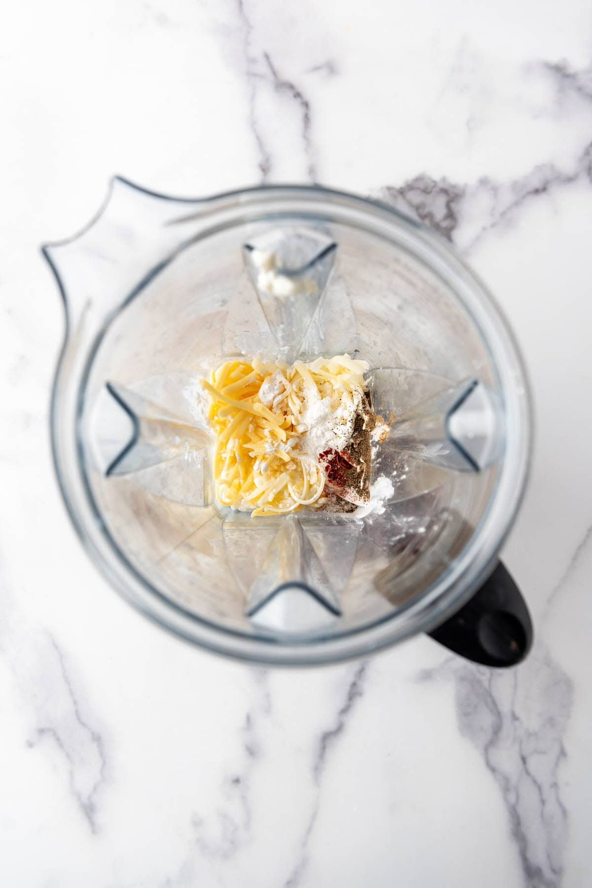 Combining grated cheese, cottage cheese, and spices in a blender.