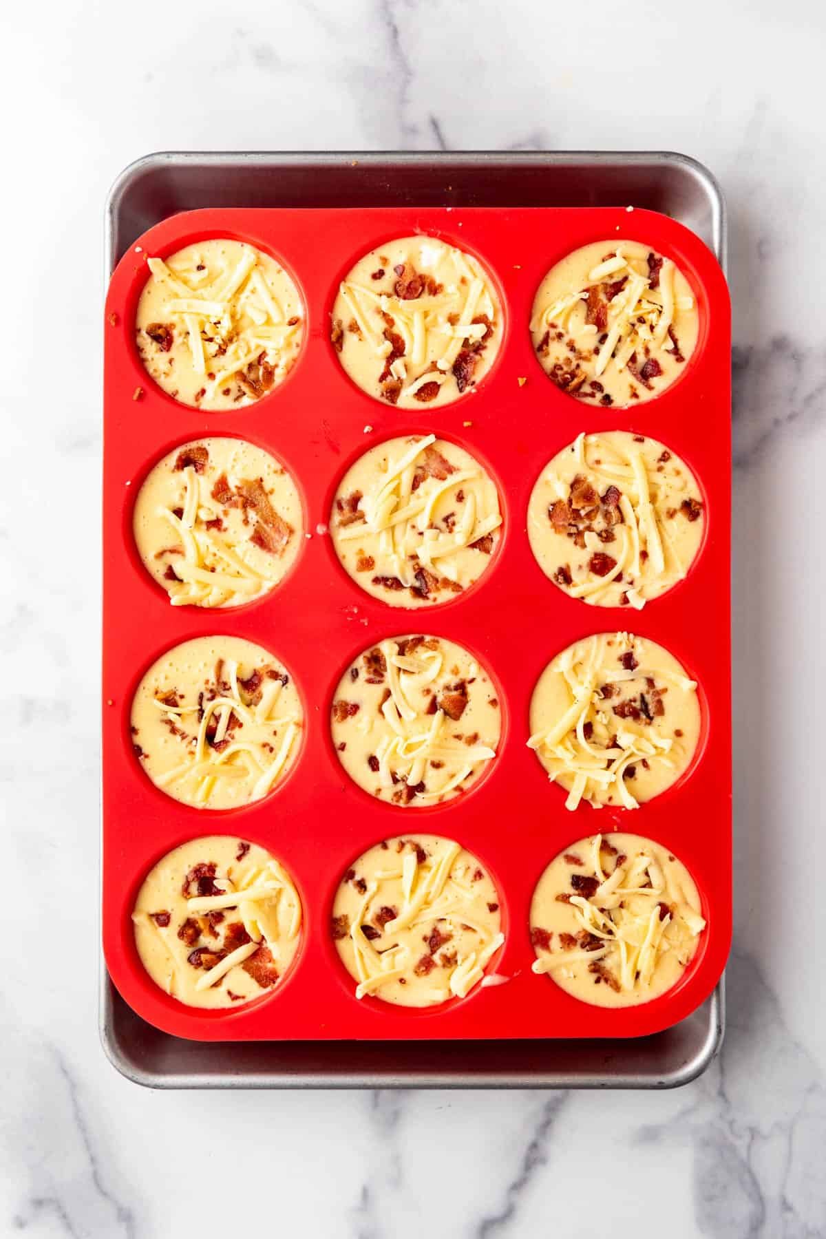 Egg bite mixture with grated cheese and crumbled bacon sprinkled on top.