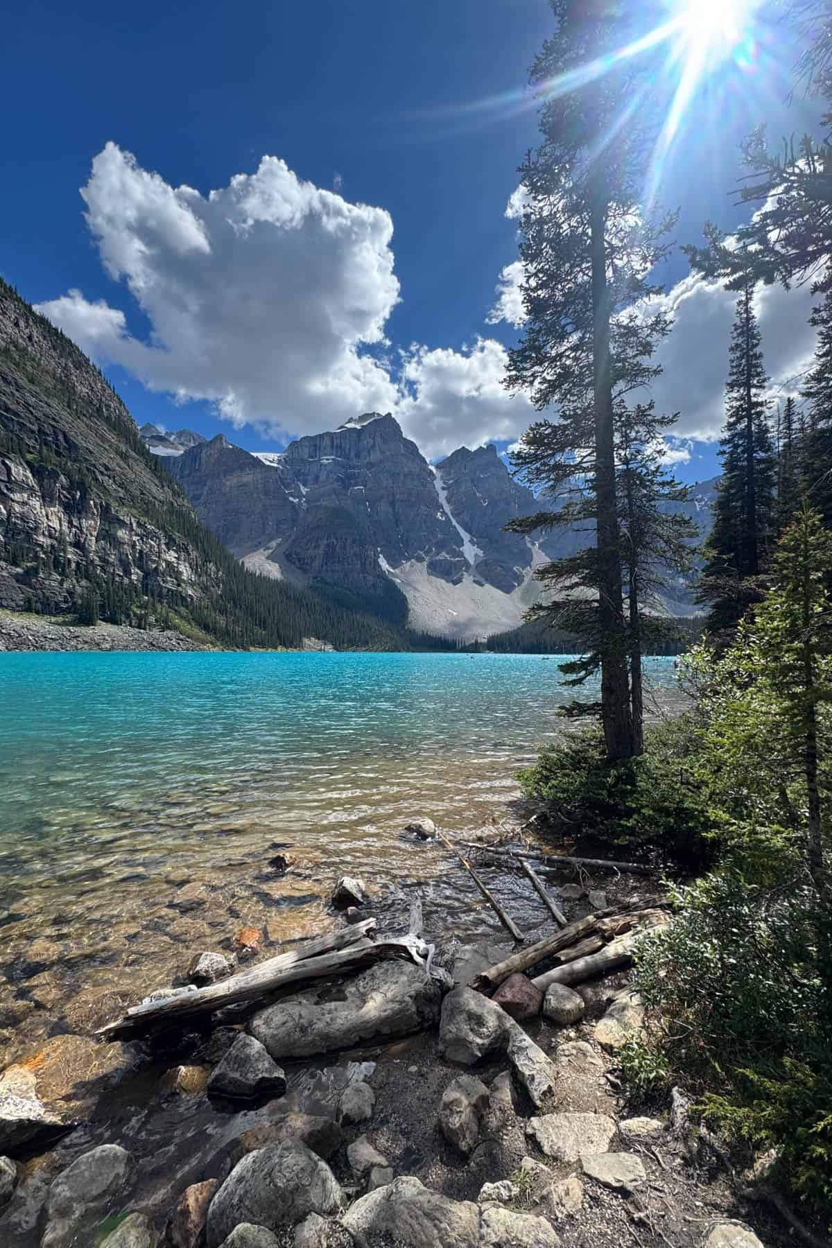 An image of Moraine Lake in Banff National Park with a blue sky, white clouds, and a shining sun.