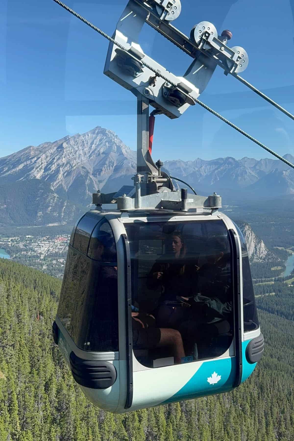 An image of the Banff Gondola going up the mountain with the trees and the town of Banff in the background.
