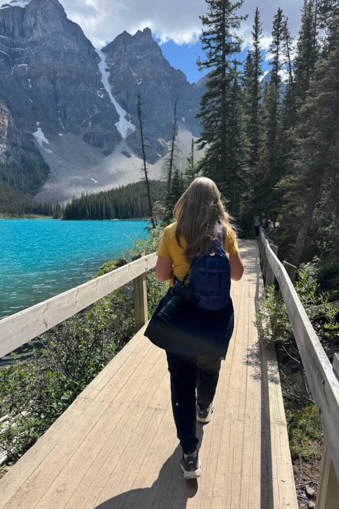 A woman walking on a board walk next to Moraine Lake in Banff National Park.