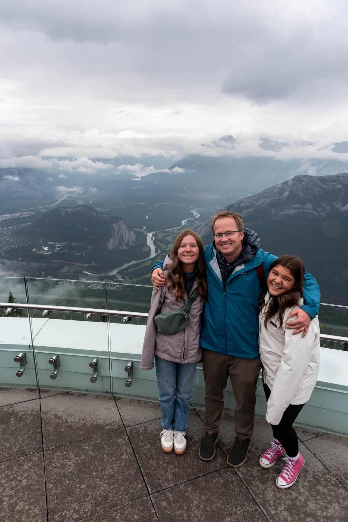 A dad and two daughters with a view of the Bow River behind them in the distance.