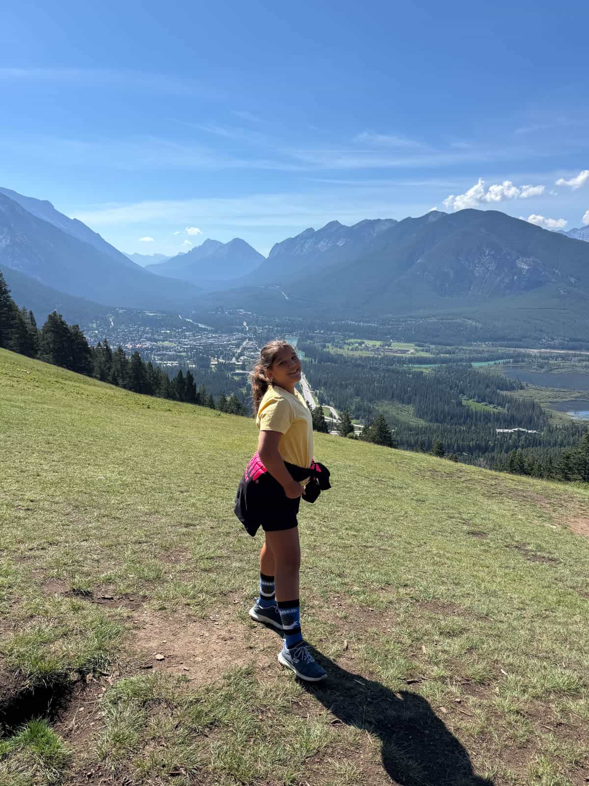 A girl standing on a mountainside with the town of Banff in the distance.