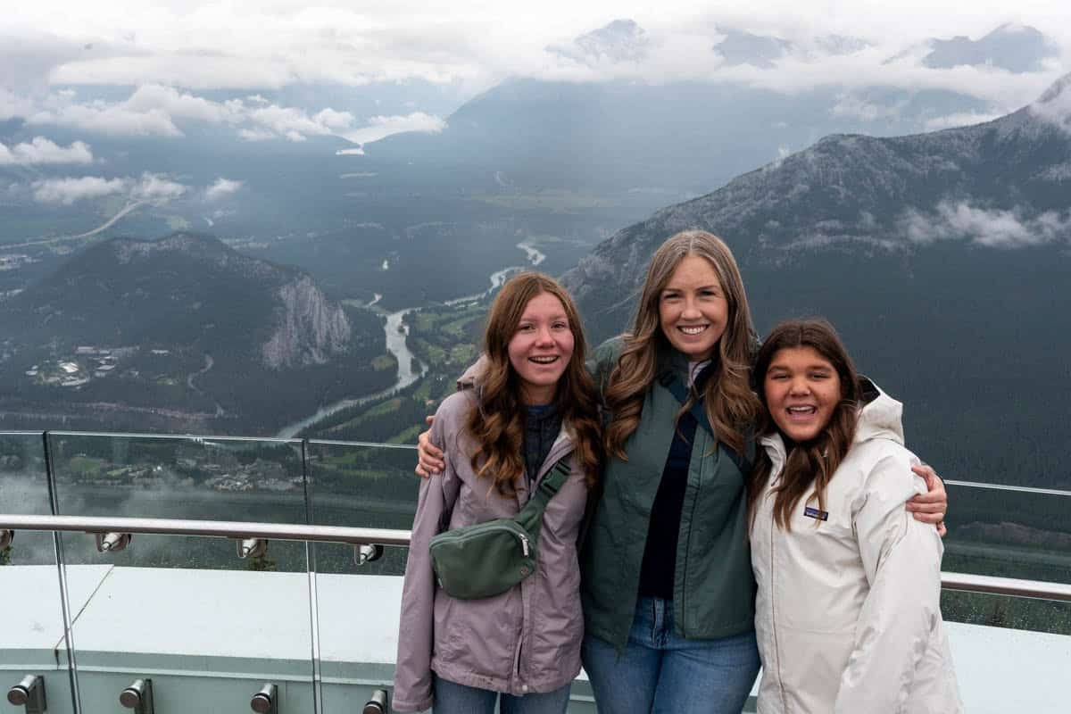 A dad and two daughters with a view of the Bow River behind them in the distance.