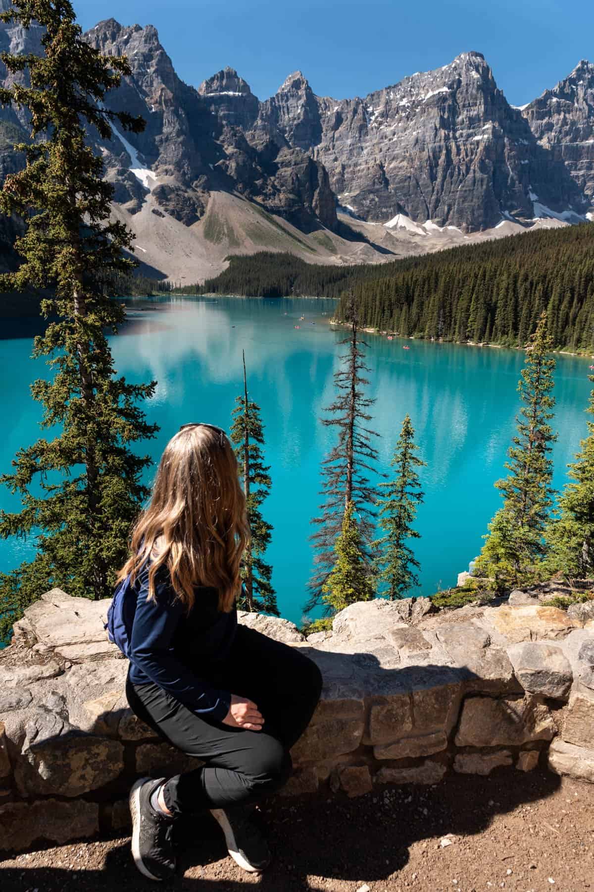 A woman sitting on rocks looking out at Moraine Lake in Canada.