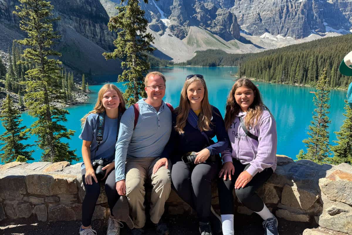 A family sitting in front of Moraine Lake with bright blue water in Banff National Park in Canada.