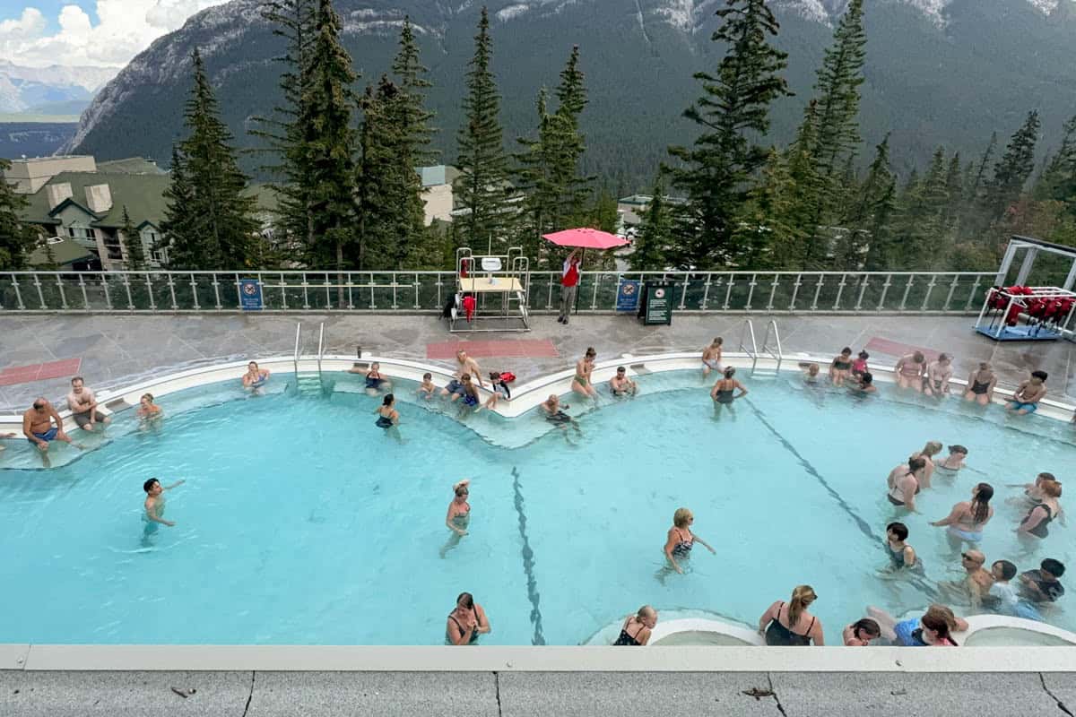 An image of a large pool with people enjoying the natural hot springs at Banff, Canada, with trees in the background.
