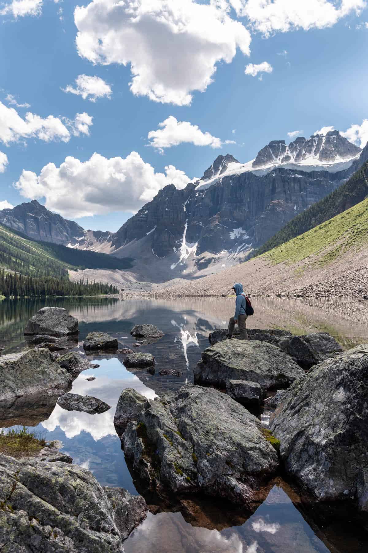 A lone figure on rocks with water all around and mountains in the background.