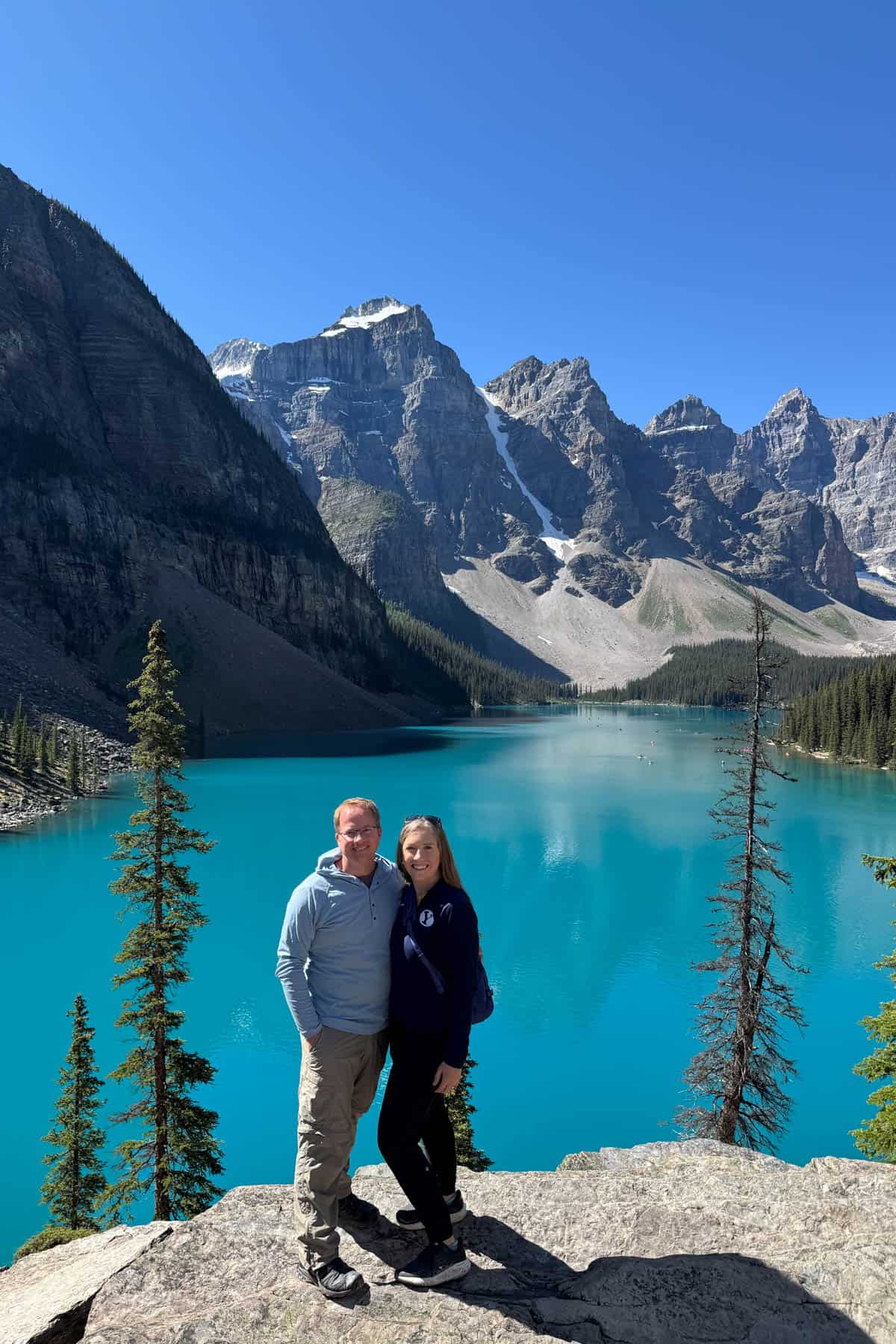 A husband and wife standing on rocks above Moraine Lake in Canada.