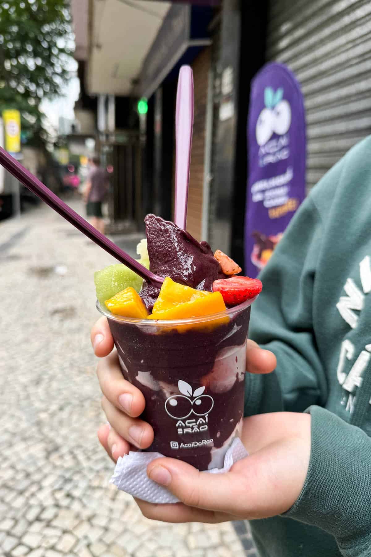 A hand holding an acai cup in Rio de Janeiro with fresh fruit on top.
