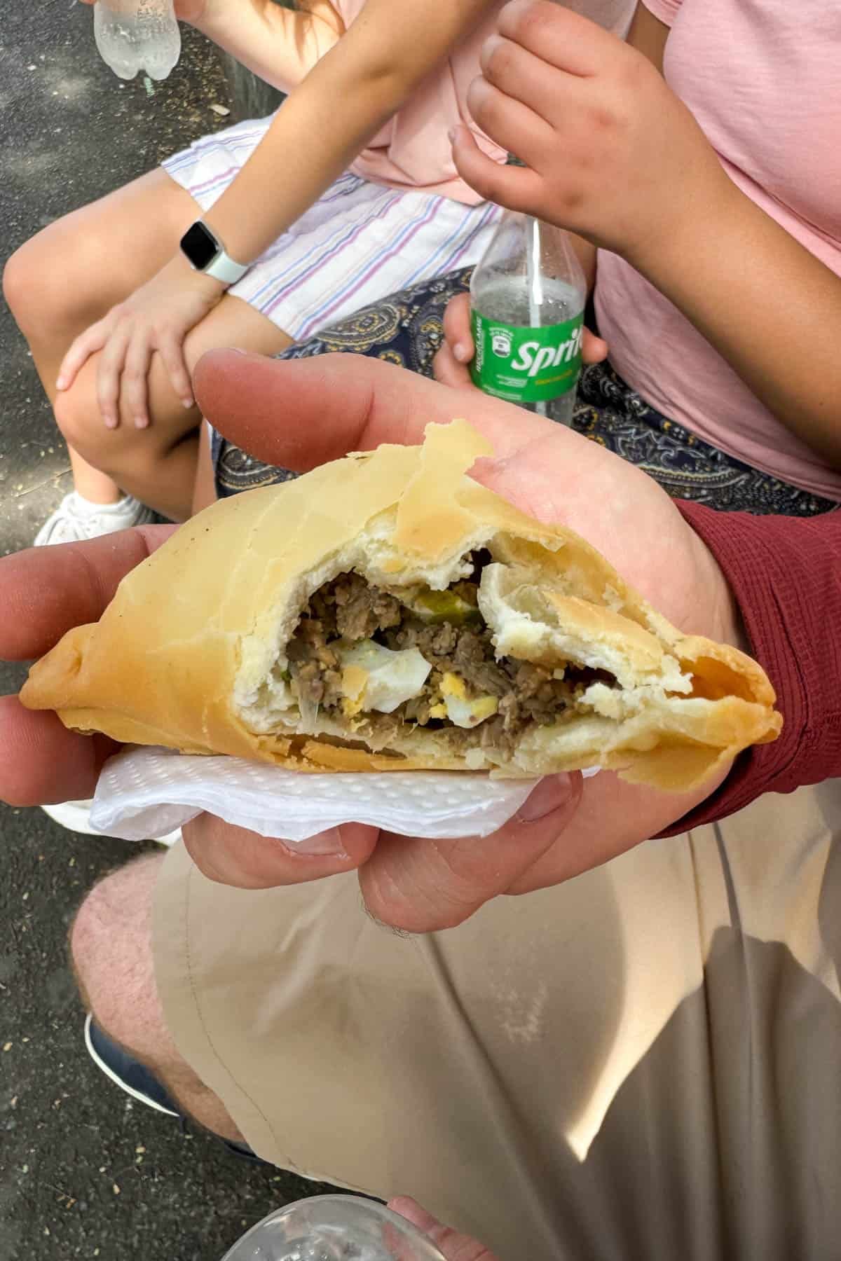 A hand holding a Paraguayan empanada with a bite taken out of it.